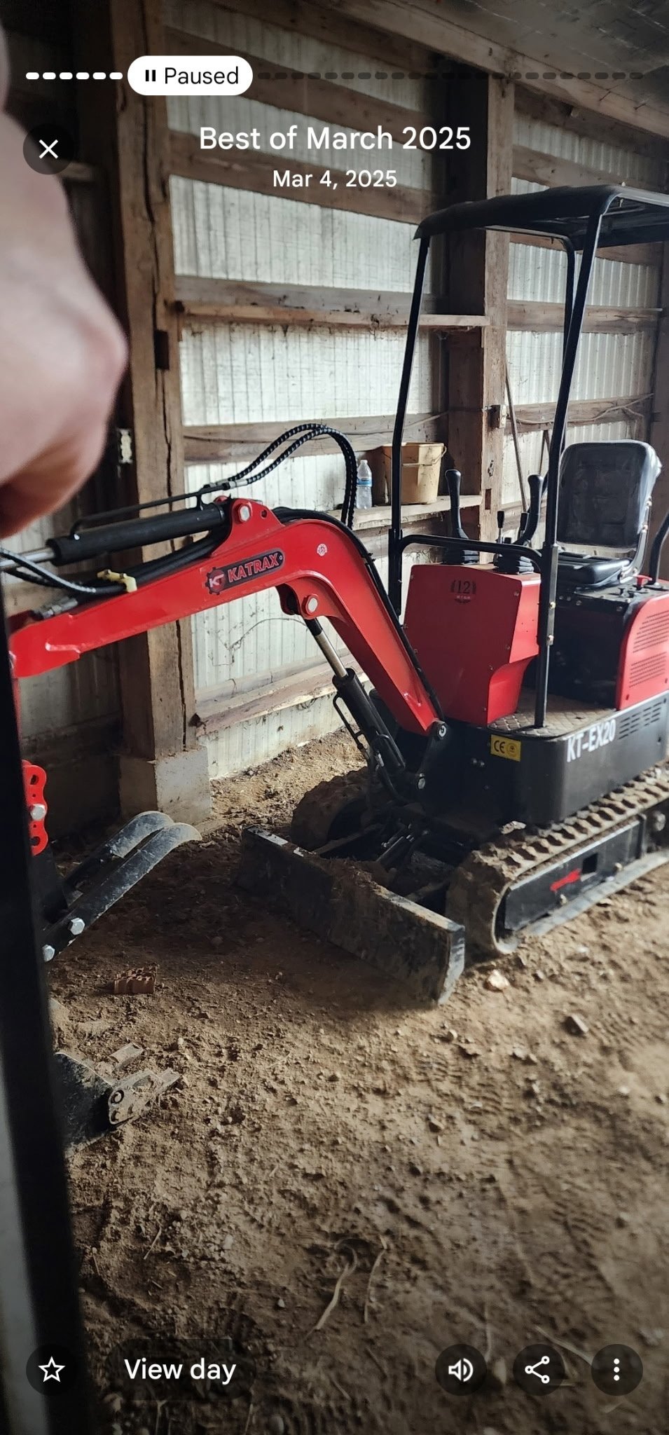 Red and black mini excavator with hydraulic arm parked in warehouse with dirt ground