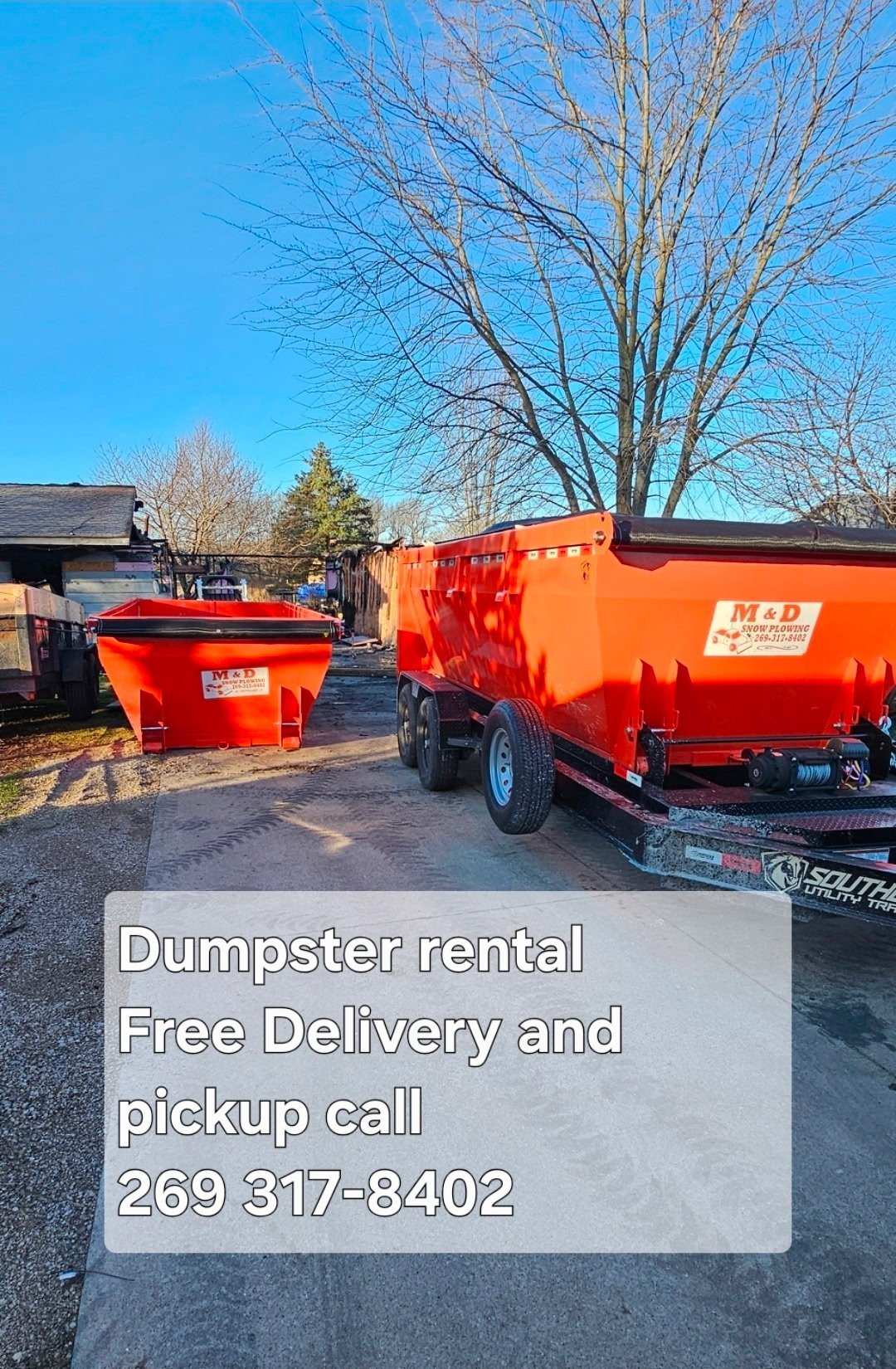 Red dumpsters at a rental service location with bare trees and blue sky, advertising free delivery and pickup with phone number
